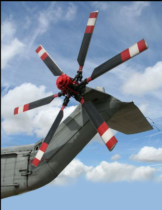 A Sikorsky S-61 conventional tail rotor photographed from below and behind: five red-and-white striped blades on an exposed hub, mounted on a canted tail pylon and driven by a shaft running aft along the tail boom.